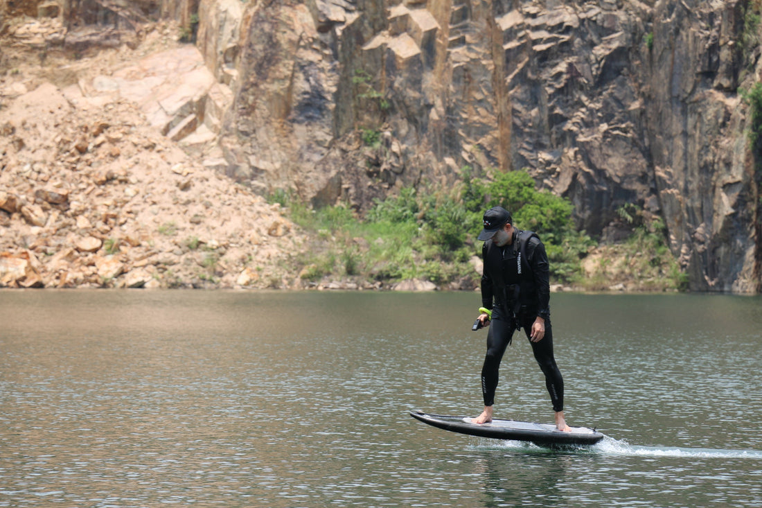 Surfers carrying ASUFUN efoil boards toward the ocean at sunset.