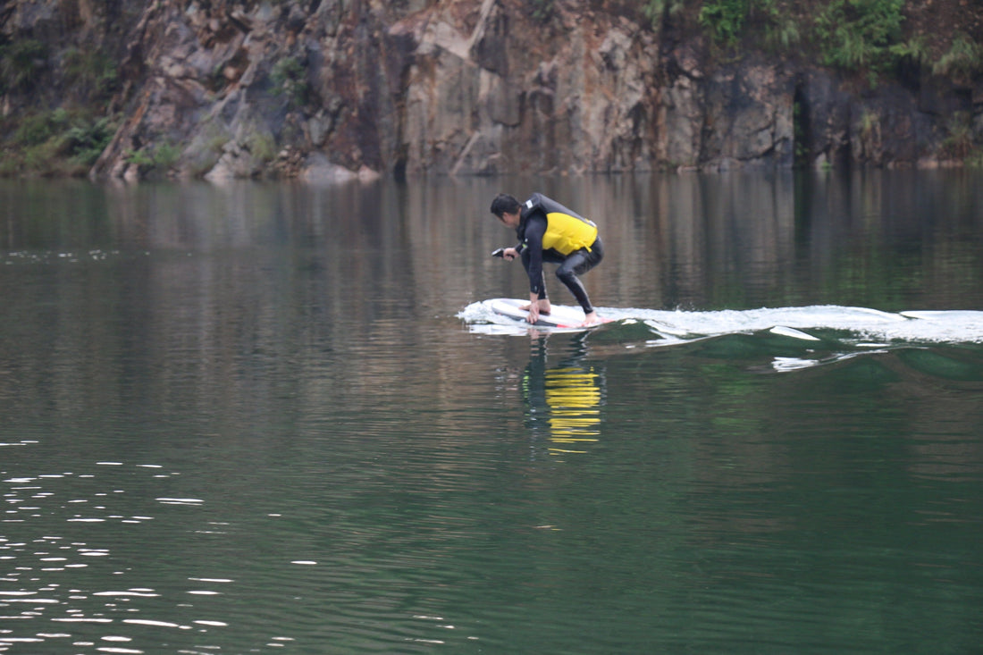 A person training on an electric hydrofoil above calm, mirror-like water, moving steadily without waves.