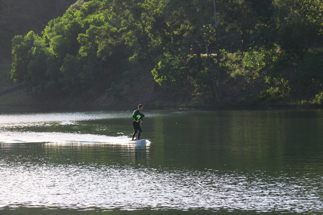 A rider gliding over calm water on a DIY hydrofoil surfboard powered by an electric drive system.